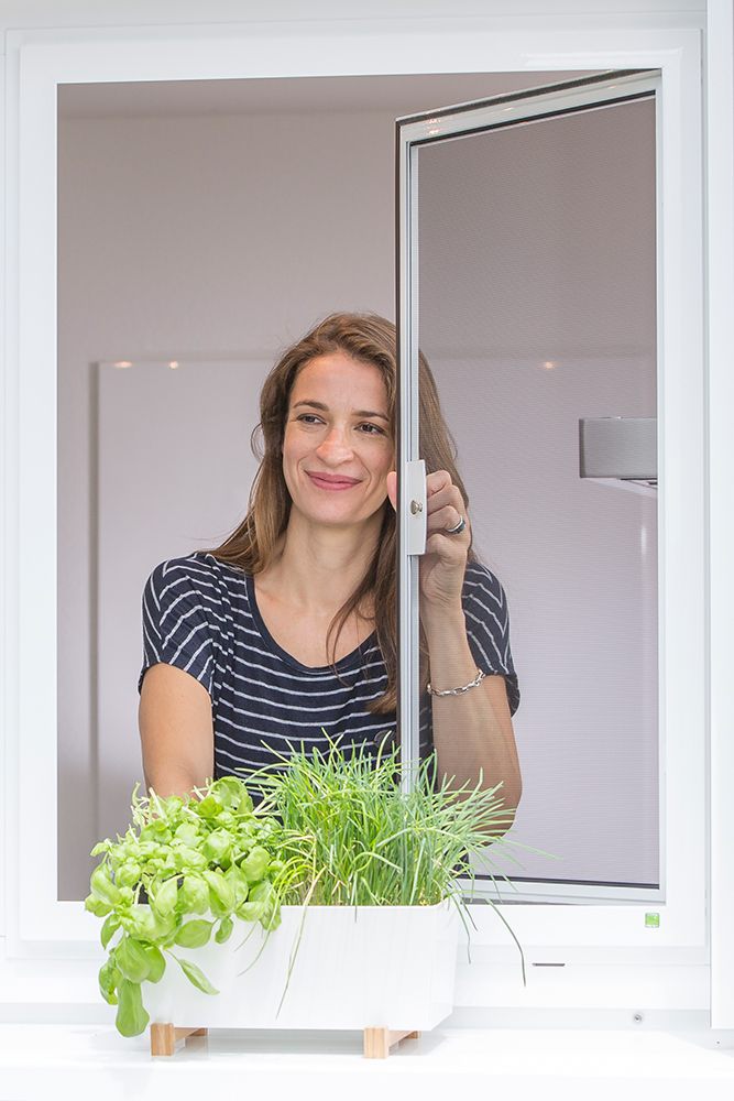 Frau, die gerade ein am Fenster montiertes Fliegenschutzgitter öffnet