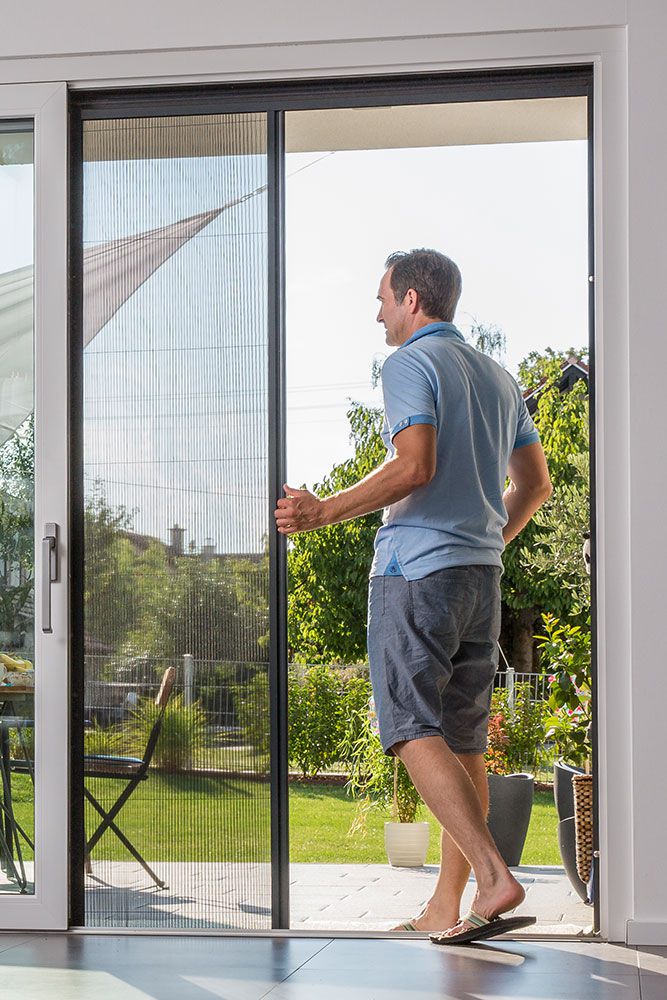 Mann, der gerade ein Plissee als Insektenschutz öffnet