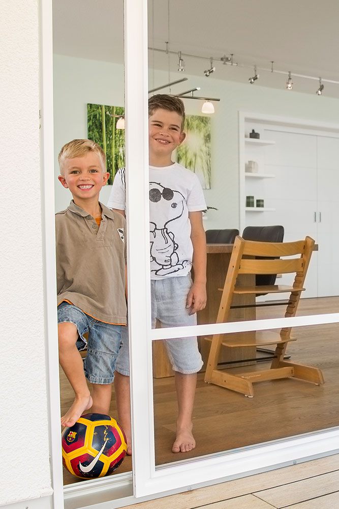Kinder die hinter einer halbgeöffnete Schiebeanlage als Insektenschutz stehen